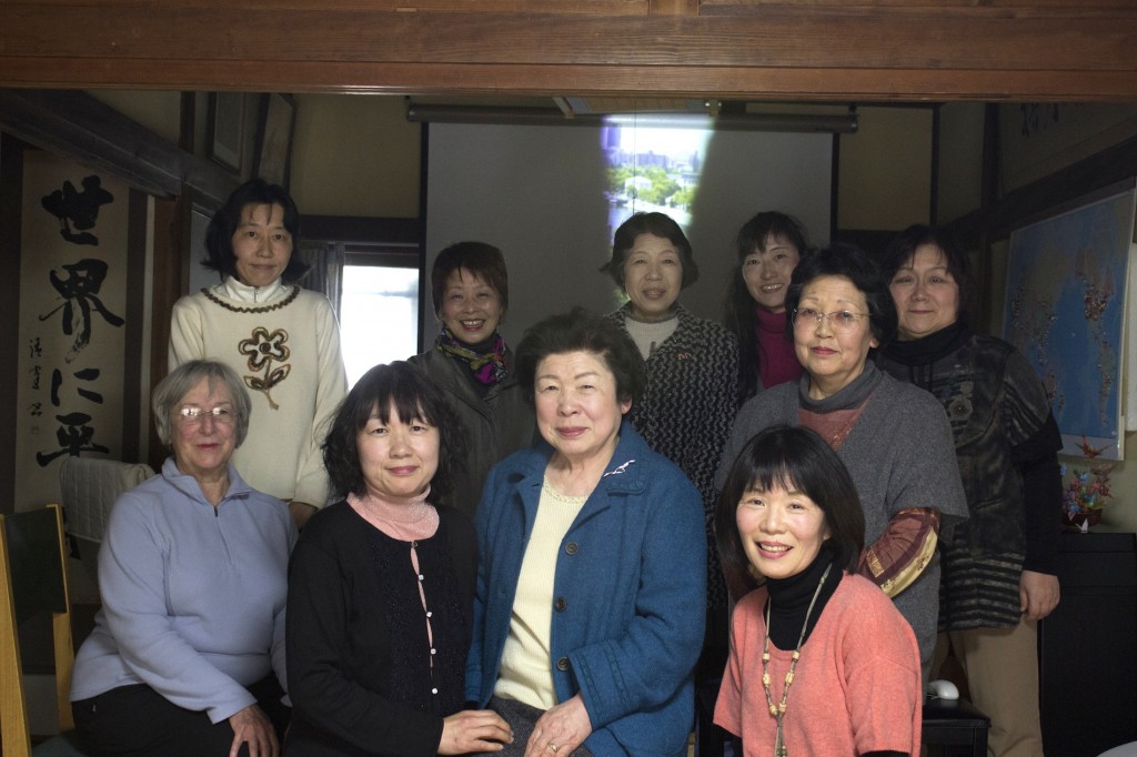 Kiyomi Kohno (front row, third from the left) and her daughter Nobuko Morikawa (front row, second from the left) sit in the main gathering room of the World Friendship Center in Hiroshima with other translators and former volunteer director, Jo Ann Sims (front row, far left).