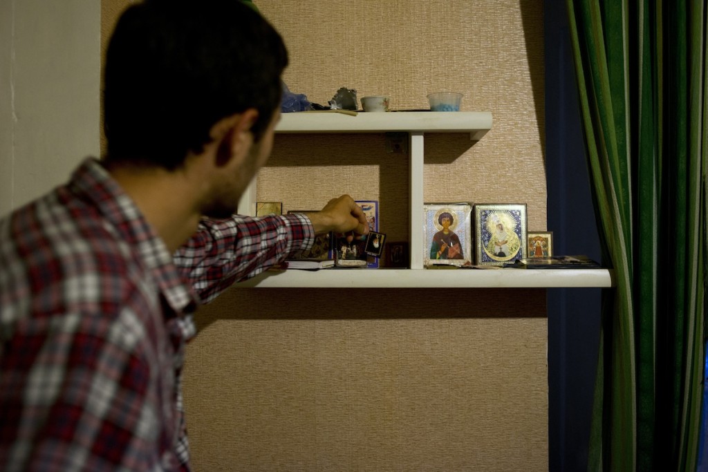 A young Georgian man adjust an icon of Patriarch Ilya on a shelf in his home in Tbilisi, Georgia on May 2, 2014. Even those who are not especially dedicated to the Orthodox Church more often than not have a number of religious icons and photos of saints in their homes.