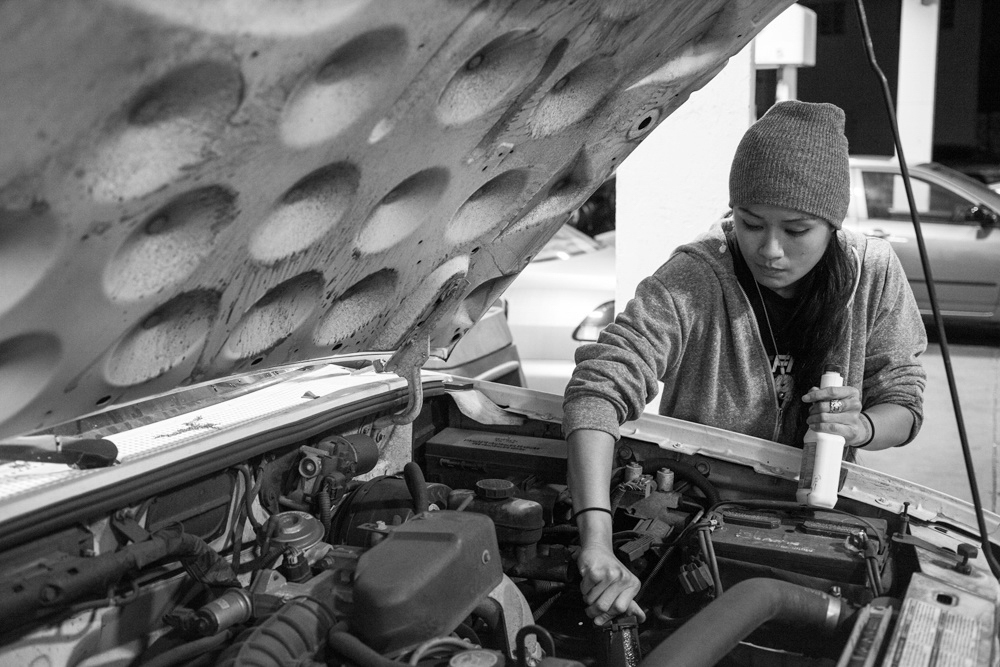 Casey pours oil under the hood of her car after stopping for gas in the SoMA district of San Francisco, CA.